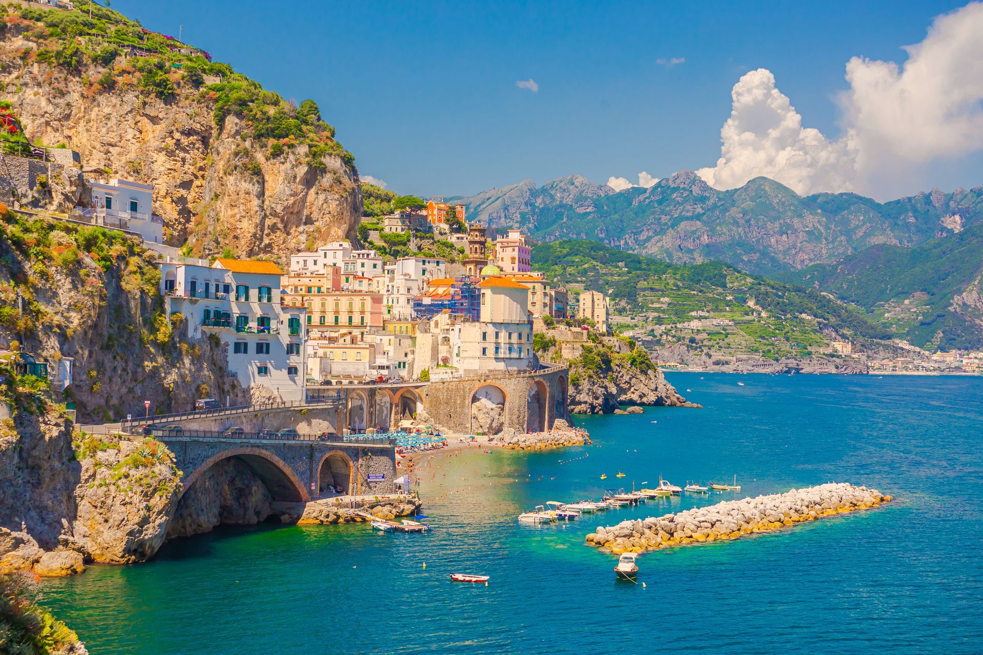 Cittadina costiera italiana con edifici arroccati su scogliere a picco sul mare turchese. Sono visibili un ponte in pietra e un frangiflutti.