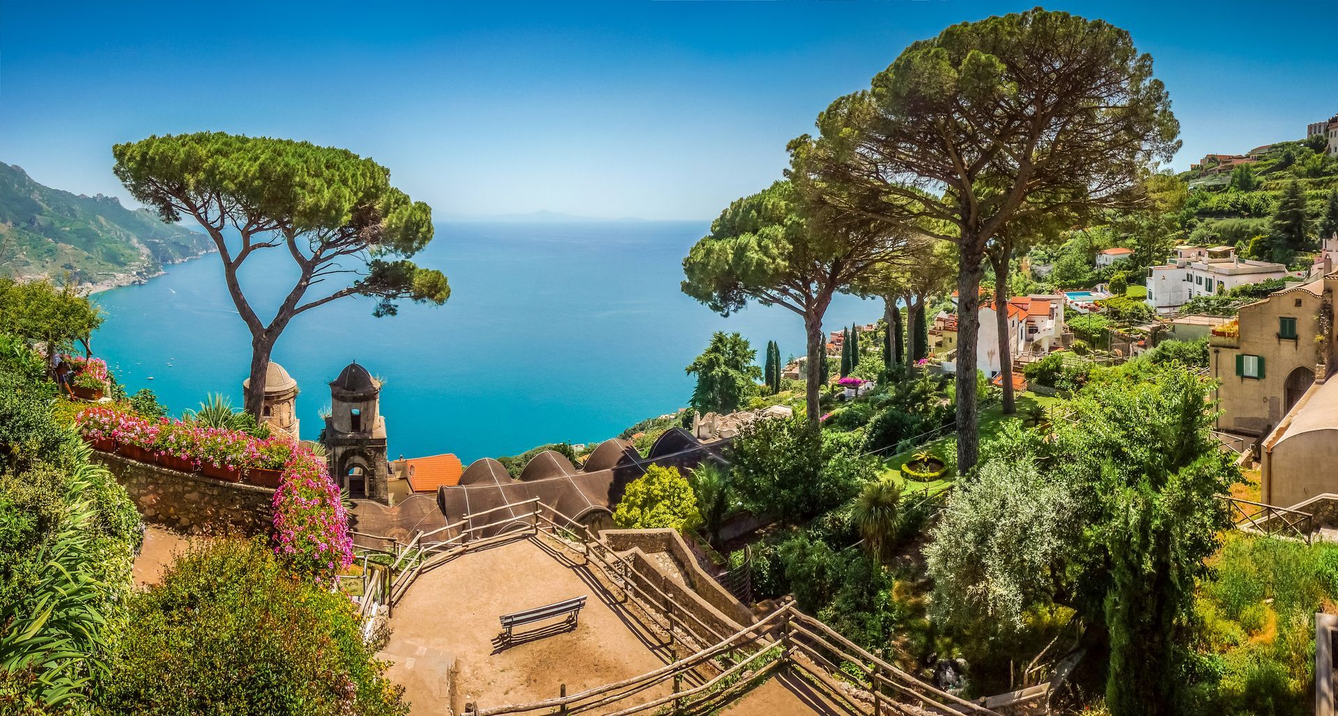 Giardini terrazzati con vista sul mare blu, con vegetazione lussureggiante ed edifici.