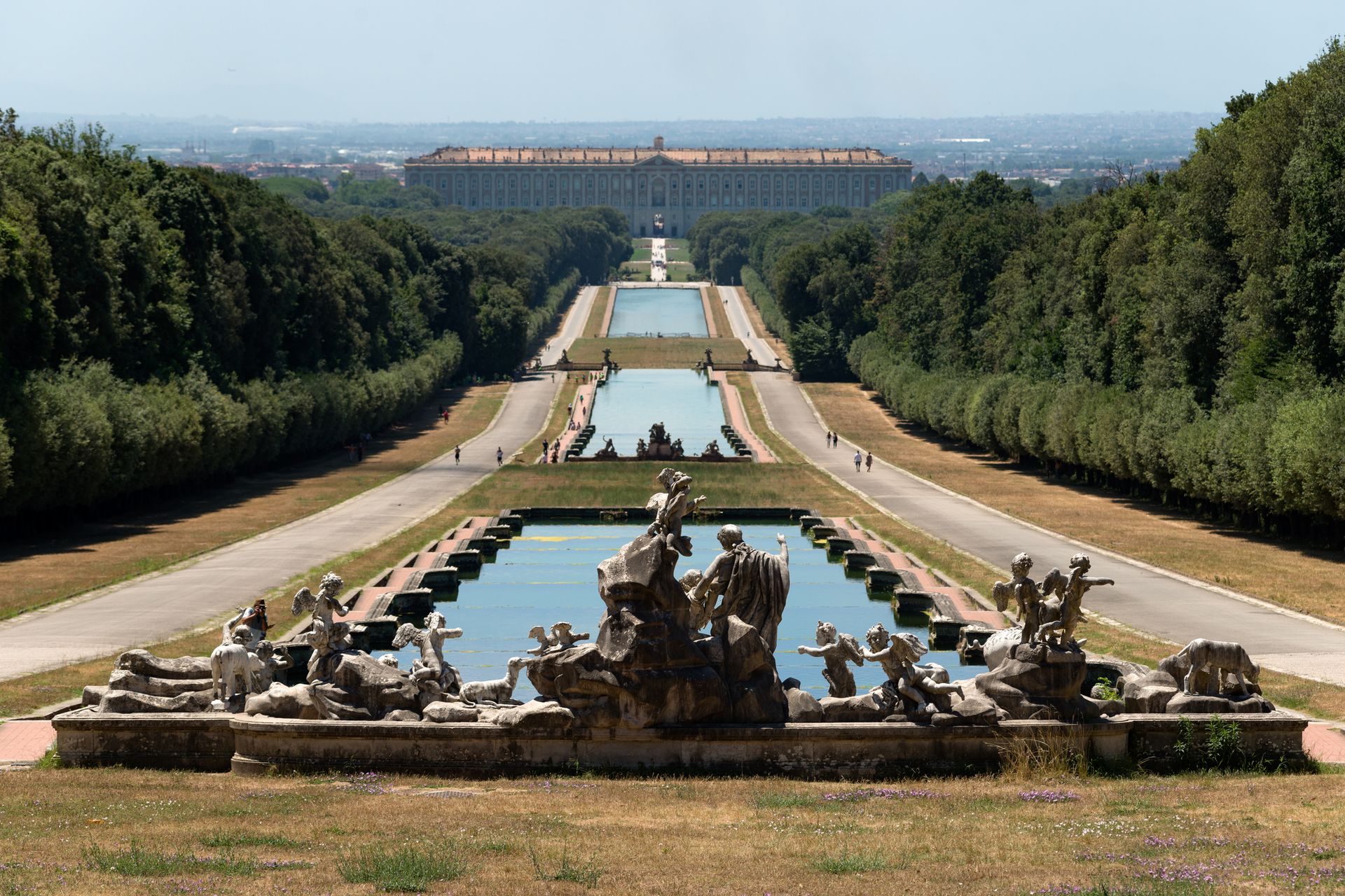 Ampia veduta della Reggia di Caserta in Italia, con un lungo corso d'acqua simmetrico e fontane che conducono al palazzo.