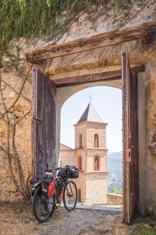 Strada tortuosa attraverso verdi colline verso una città costiera con torri, sotto un cielo azzurro e limpido.