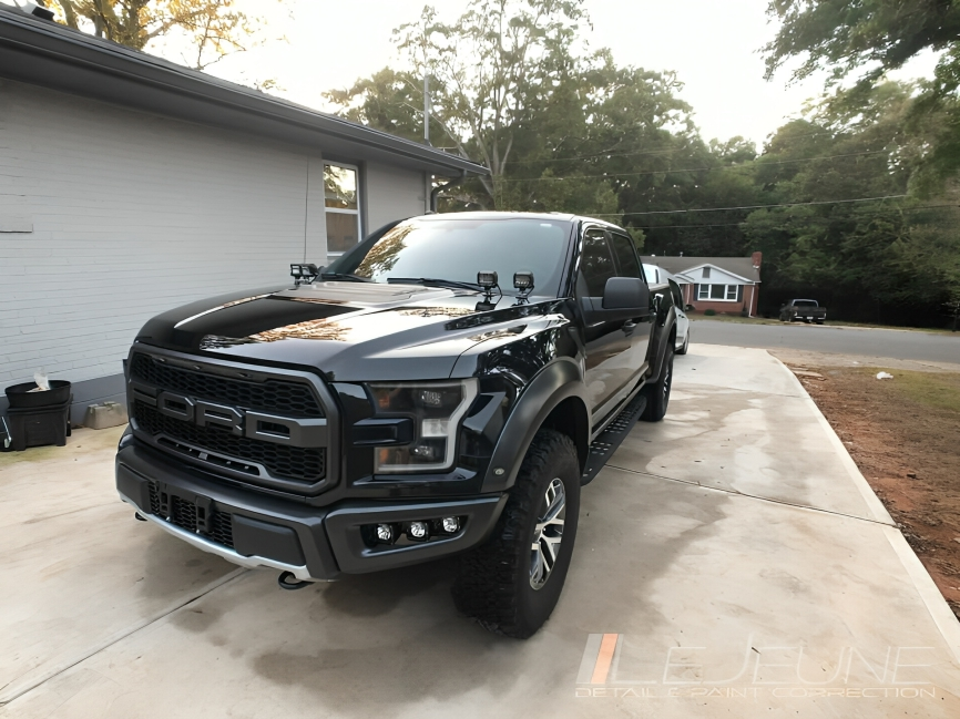 Black Ford Raptor truck parked on a concrete driveway in front of a house.