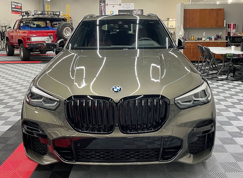 A bmw x5 is parked in a garage with a jeep in the background.