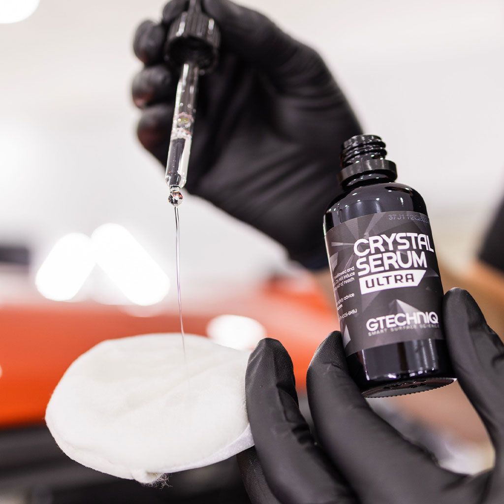 A person is holding a bottle of crystal serum ultra and a dropper.