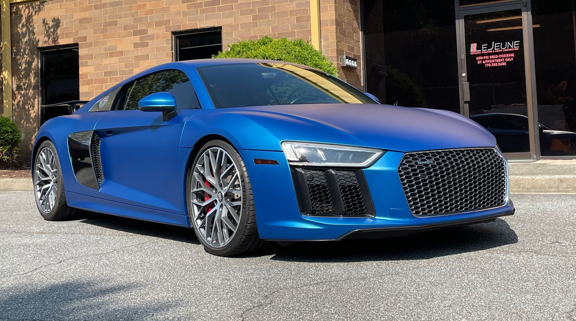 A blue audi r8 is parked in front of a building.