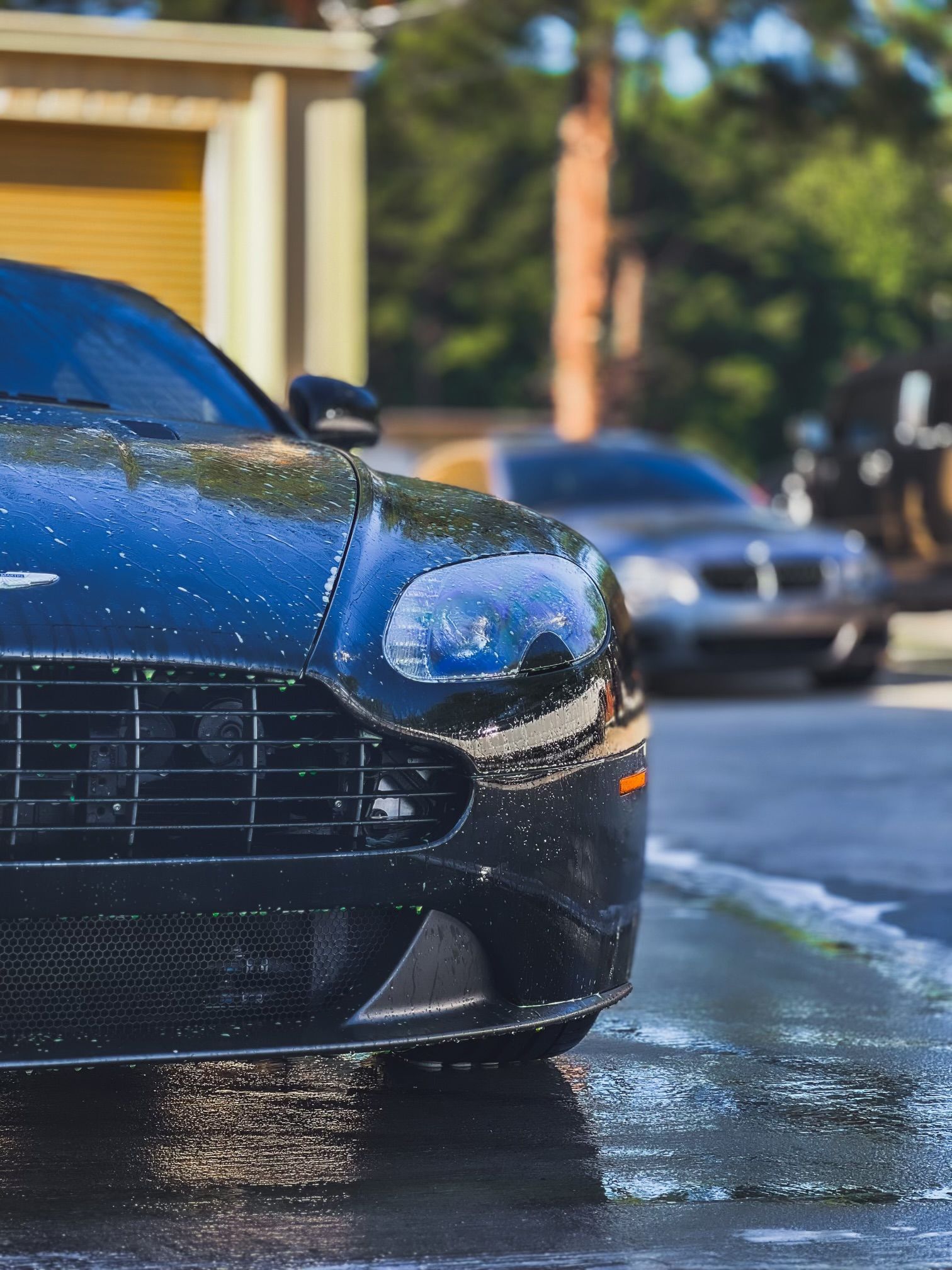 A black car is parked on the side of the road in the rain.