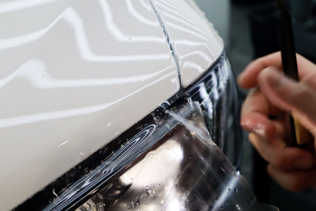 A person is applying a protective film to the headlight of a car.