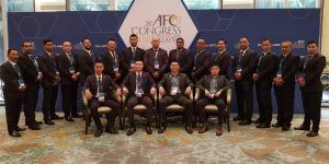 Group photo of men in suits, posed in front of a blue backdrop with the 