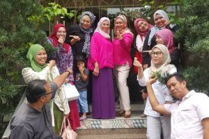 Group of people posing on steps, mostly women in colorful headscarves and clothing, some making hand gestures, outdoor setting.