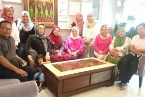 Group of people, mostly women in headscarves, sitting and standing together indoors. Some are smiling, with a young child in front.