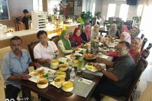 Group of people seated around a table in a restaurant, eating food and smiling. Some women wear headscarves.