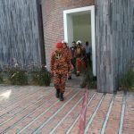 Firefighter in orange gear walks towards a doorway with others inside a brick building.
