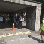People walking in a covered entryway. A traffic cone and yellow tactile paving are in the foreground.