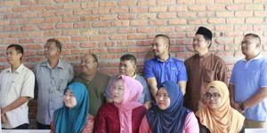 A group of people pose in front of a brick wall. Several women wear hijabs, and men wear various shirts.