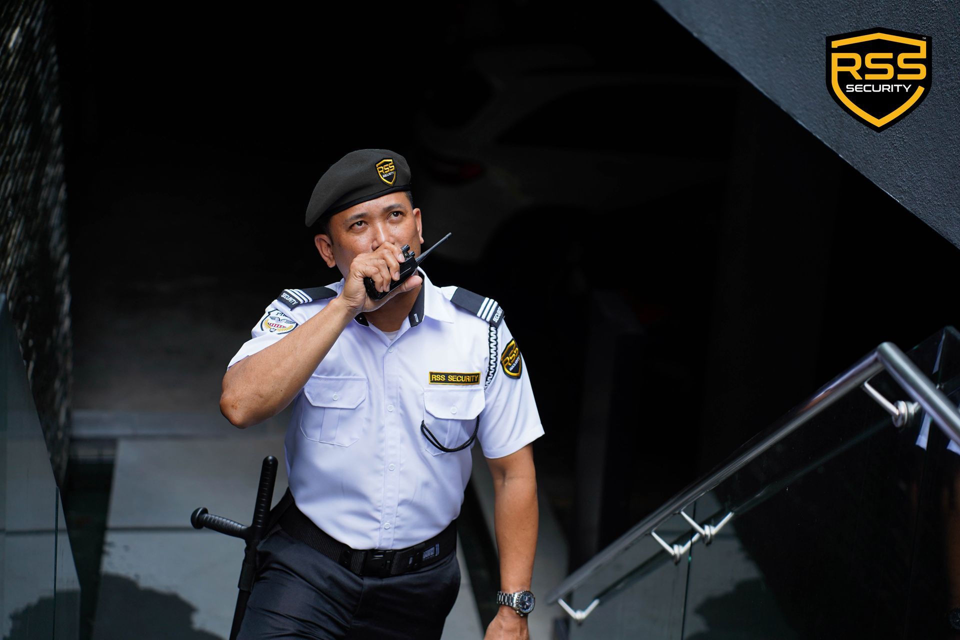 A supervisor in a black uniform briefing four security personnel in white shirts and black trousers in an outdoor lot.