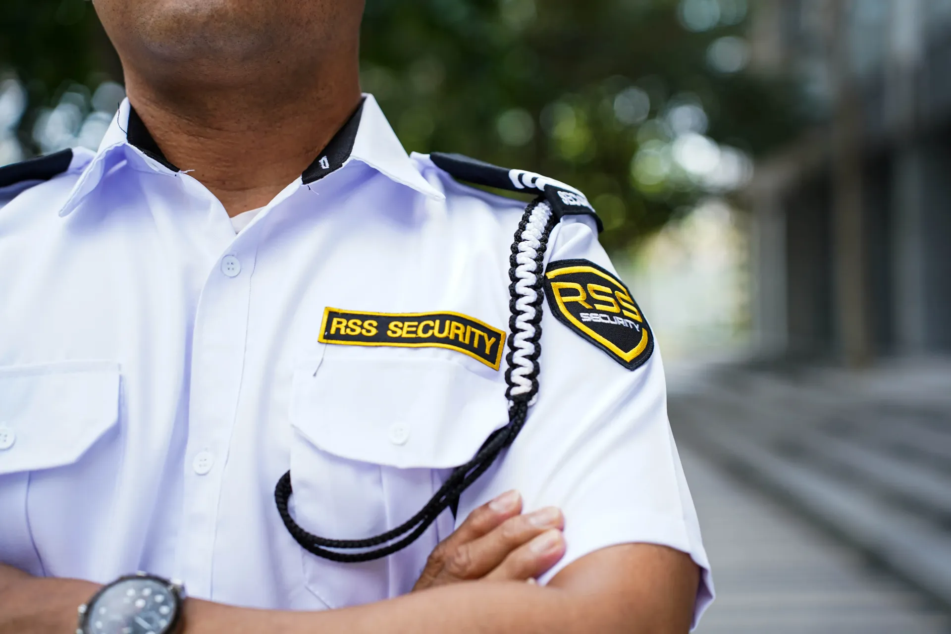 Five security personnel in white uniforms and black berets stand with arms crossed in front of a modern building.