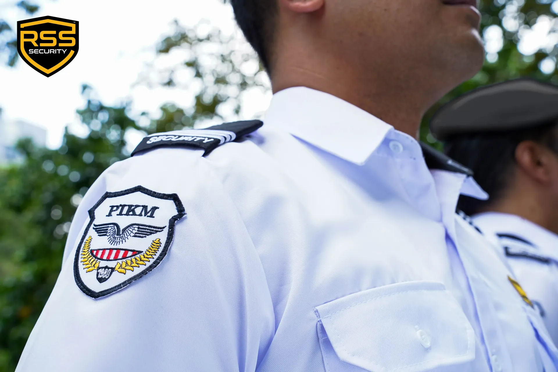 A supervisor in a black uniform briefing four security personnel in white shirts and black trousers in an outdoor lot.