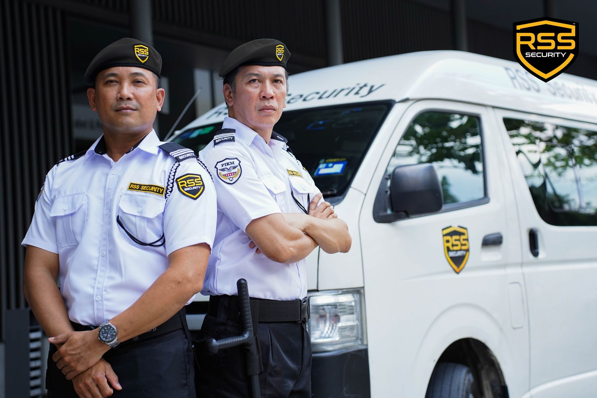Five security personnel in white uniforms and black berets stand with arms crossed in front of a modern building.