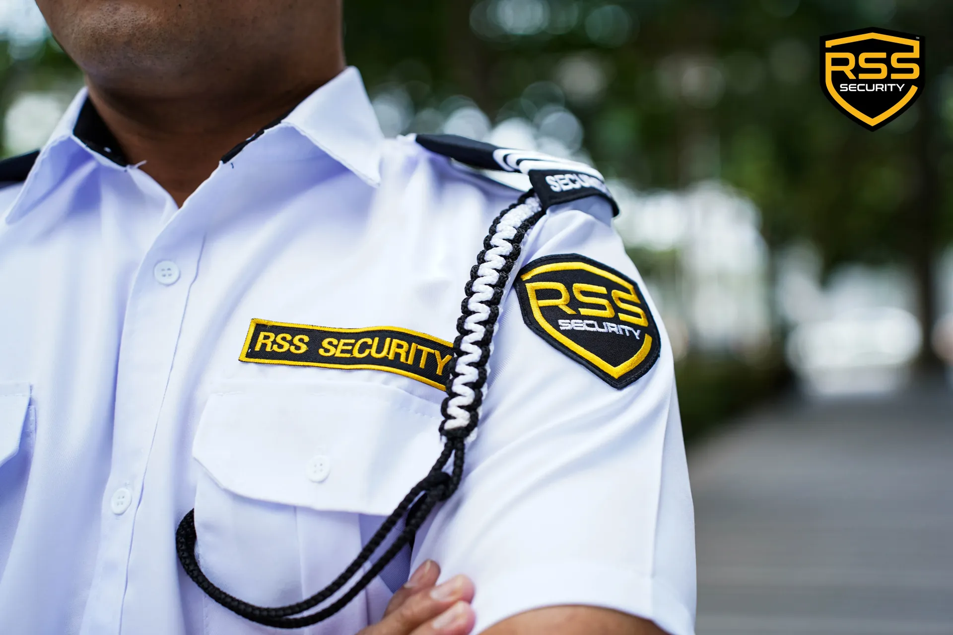 Security guard in white uniform with RSS patches and black shoulder cord.