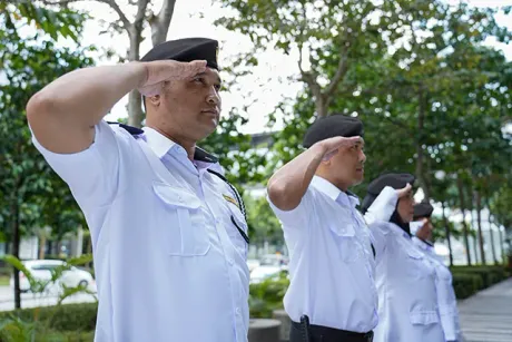 Four uniformed people in white shirts and blue berets saluting outdoors.