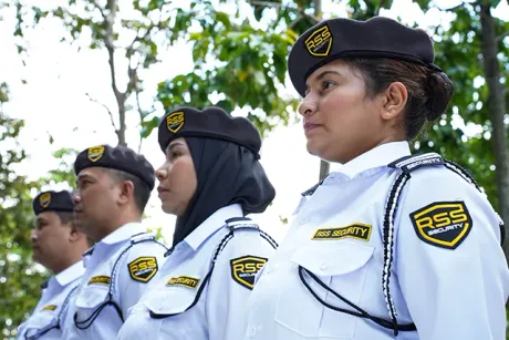 Four security personnel in white uniforms and blue berets stand outdoors, looking right. 