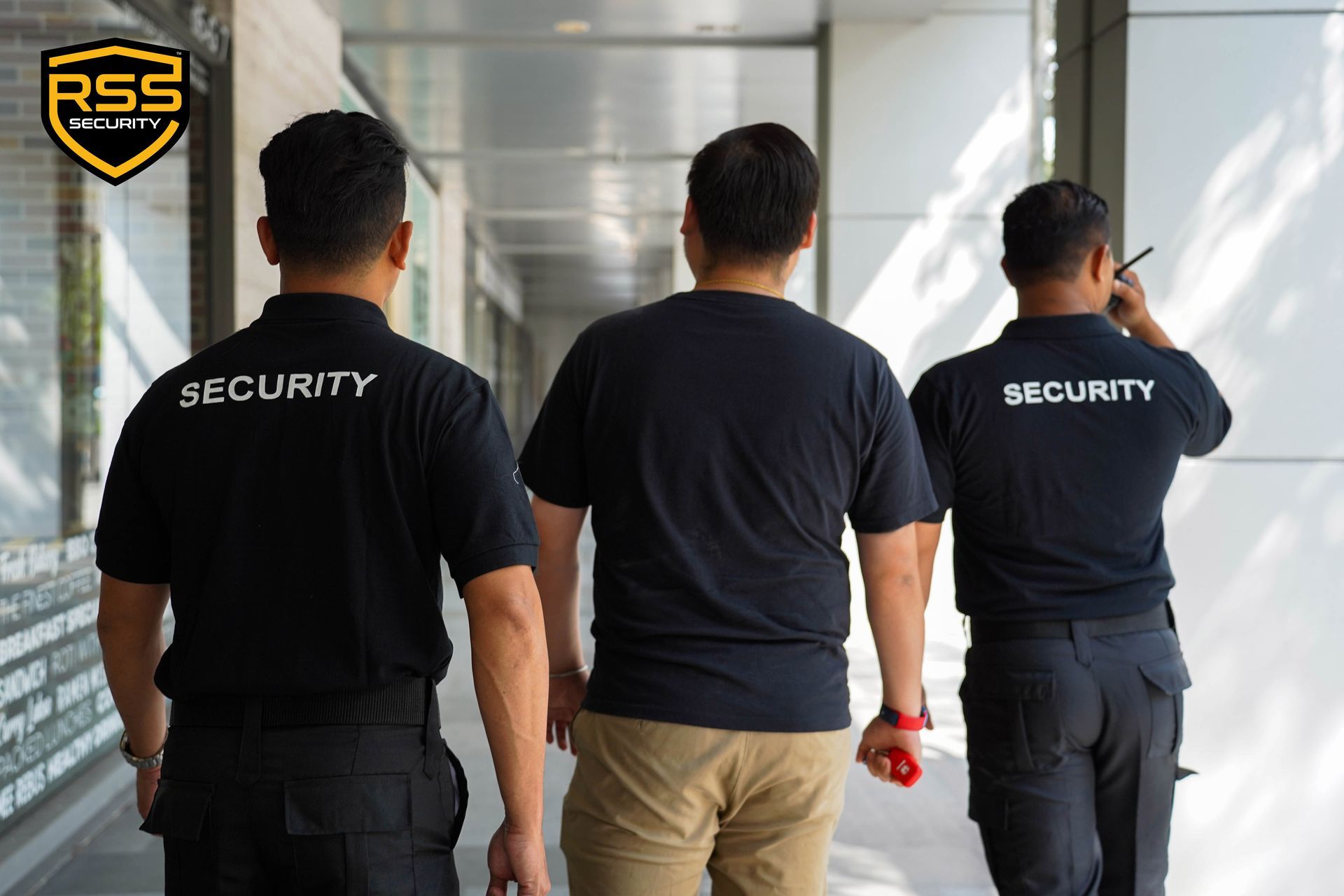 A supervisor in a black uniform briefing four security personnel in white shirts and black trousers in an outdoor lot.