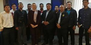 A group of men and a woman in a headscarf posing together indoors. They are standing and smiling.