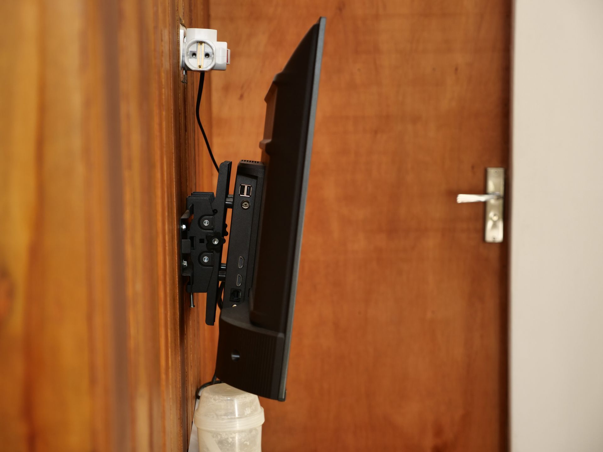 A black television monitor mounted on a wooden wall, with a power cable connected to a nearby wall outlet.