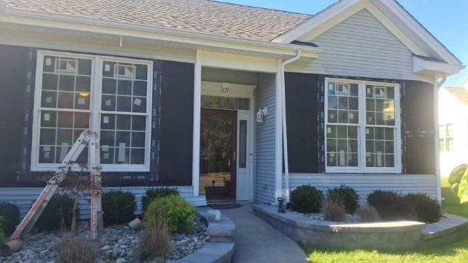 A wooden deck with railings extends from a gray house toward a backyard with tall trees and a small garden shed.
