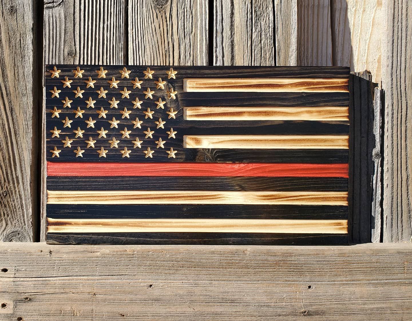 Wooden American flag with red line for firefighters, set against a weathered wooden background.
