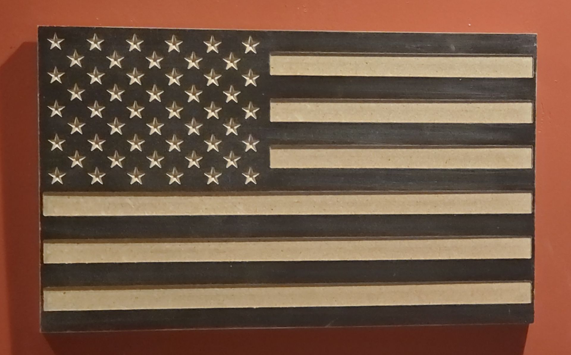 Wooden American flag with carved stars and stripes, hanging on a wall.