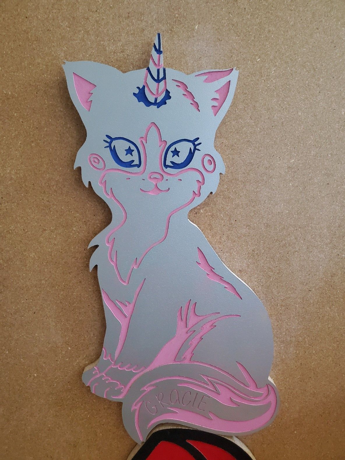 Gray cat-unicorn with pink accents, smiling, sitting.