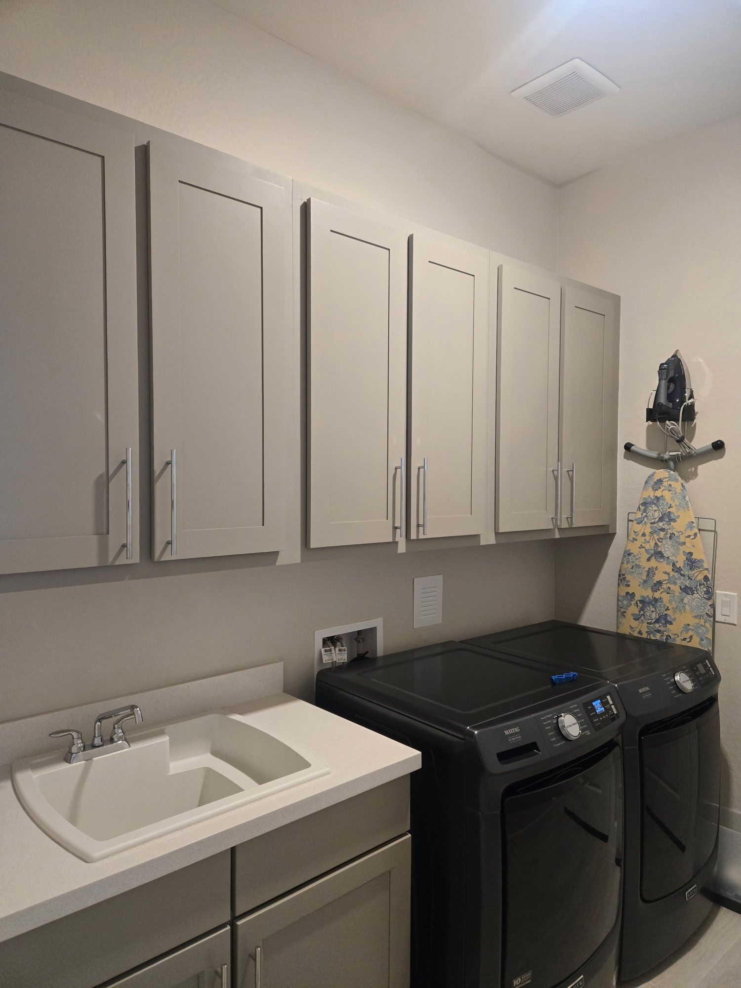 Laundry room with gray cabinets, black washer/dryer, and a sink.