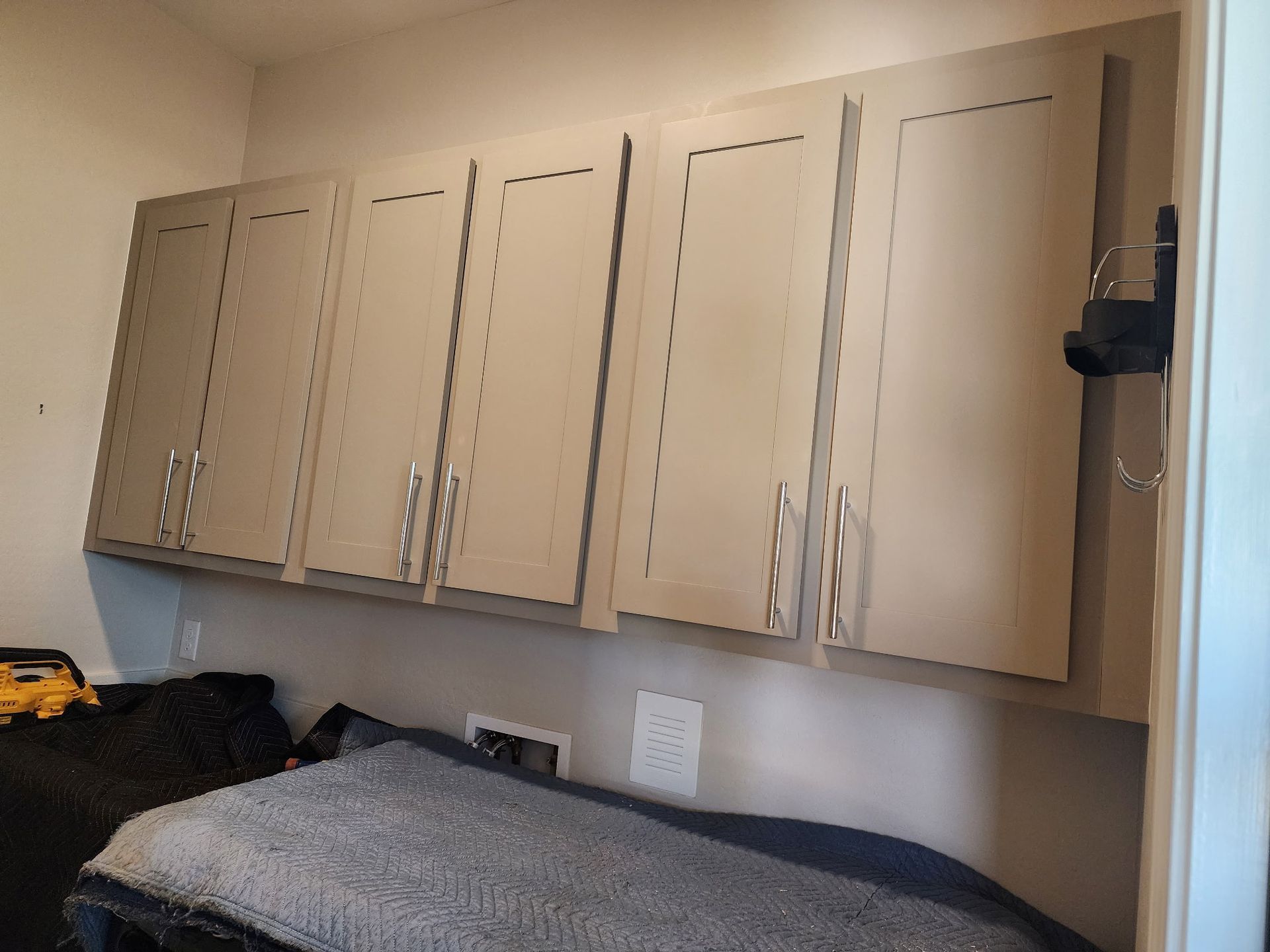 Four tan-colored upper cabinets mounted on a neutral wall. Silver handles, and a gray blanket below.