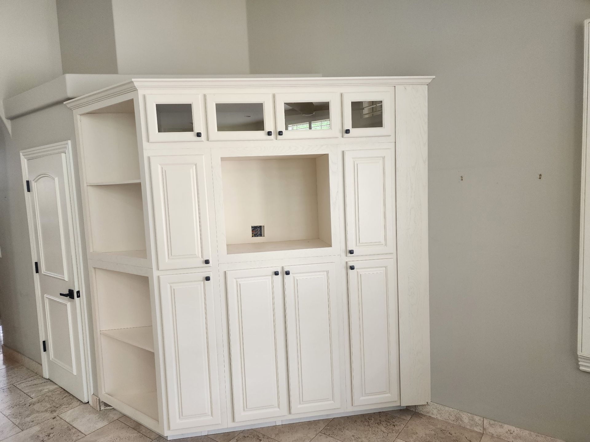 White built-in cabinet unit with a recessed TV space, shelves, and door against a gray wall.