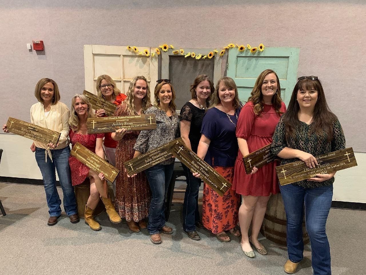 Group of women smiling, holding awards, in front of a decorative door.