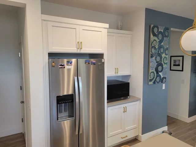 White kitchen cabinets frame a stainless steel refrigerator and microwave, with a blue accent wall.