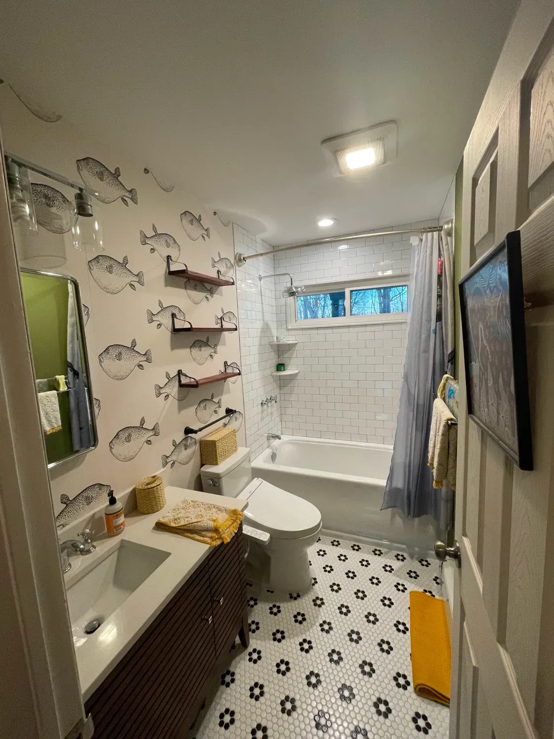 Bathroom with fish-print wallpaper, black and white floor tiles, and a white bathtub.