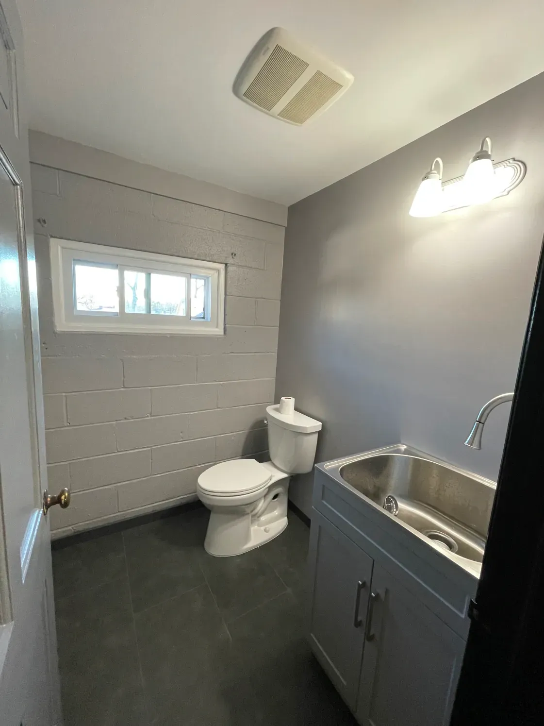 Small gray bathroom with toilet, sink, and window.