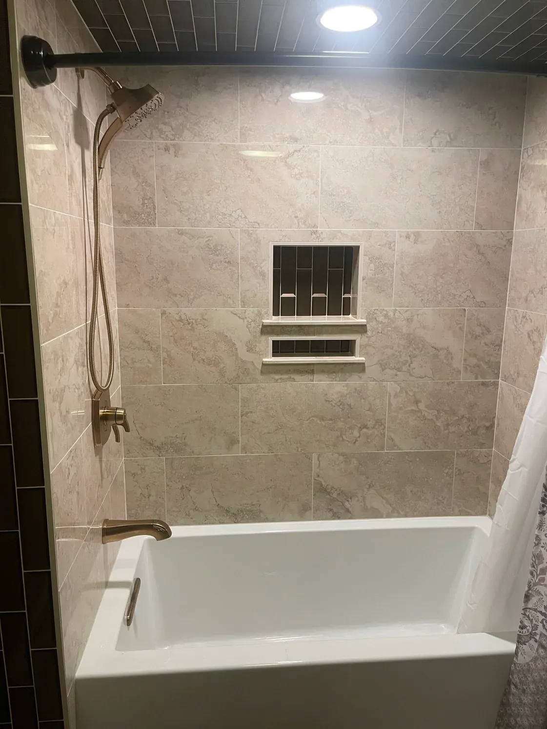 Bathroom with a white bathtub, beige tiled walls, and gold shower fixtures.