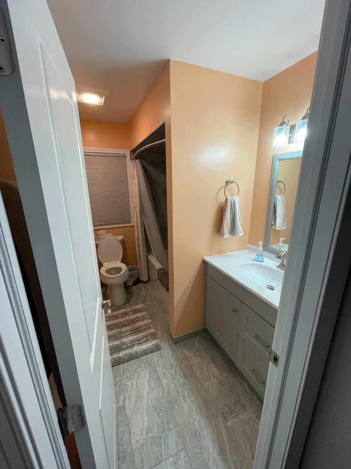 Narrow bathroom with orange walls, white vanity, and toilet. Gray tile floor.
