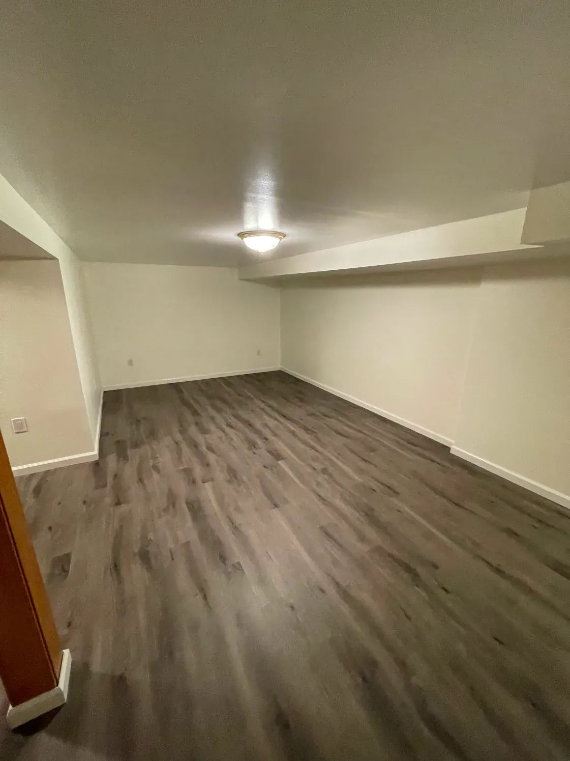 Empty basement room with gray wood-look flooring and cream-colored walls.