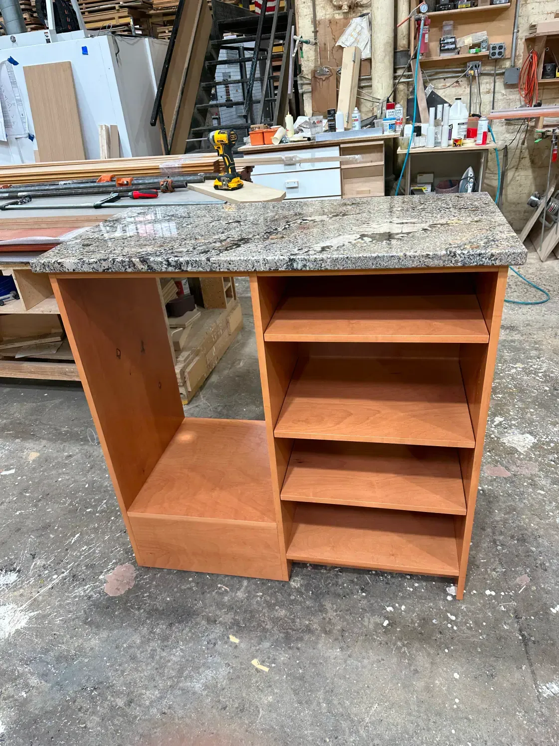 A kitchen island with granite countertop and open shelves, in a workshop setting.