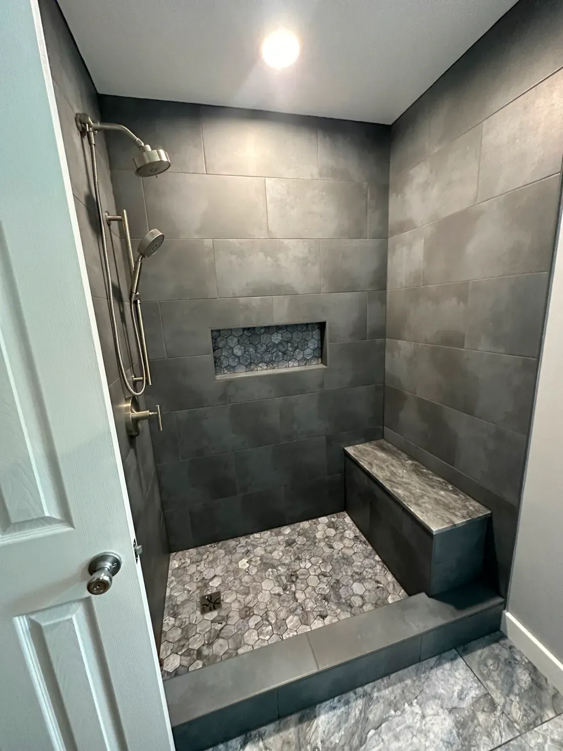 Dark tiled shower with stone floor, a built-in bench, and a niche with decorative stones.