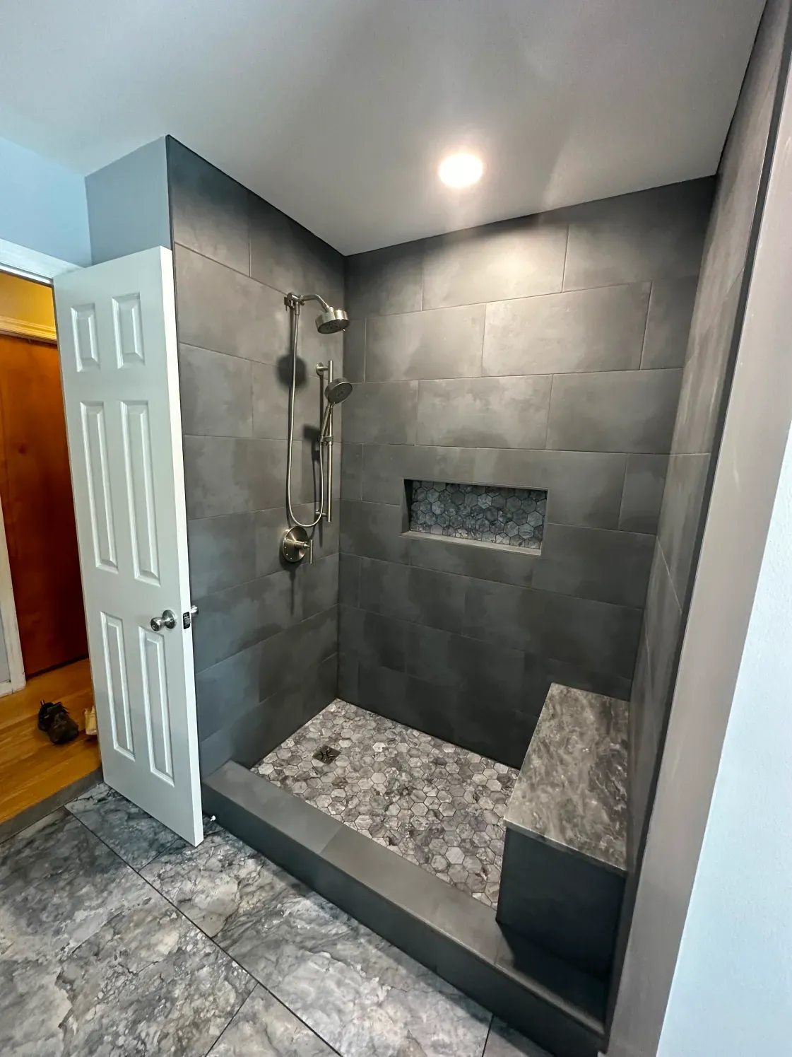 Gray tiled walk-in shower with pebble floor, built-in bench and niche.