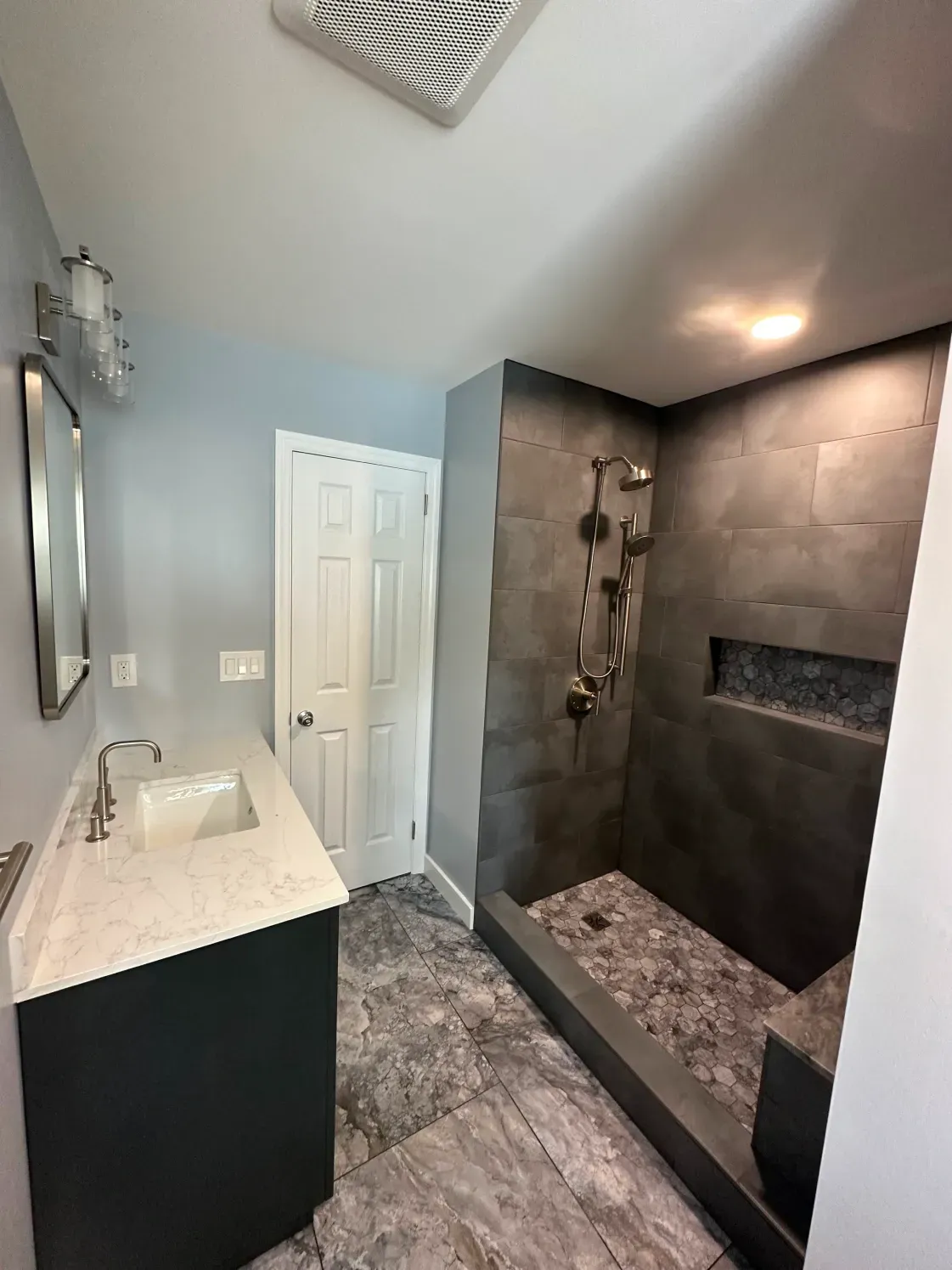 Modern bathroom with gray tile shower, dark vanity, and blue walls.
