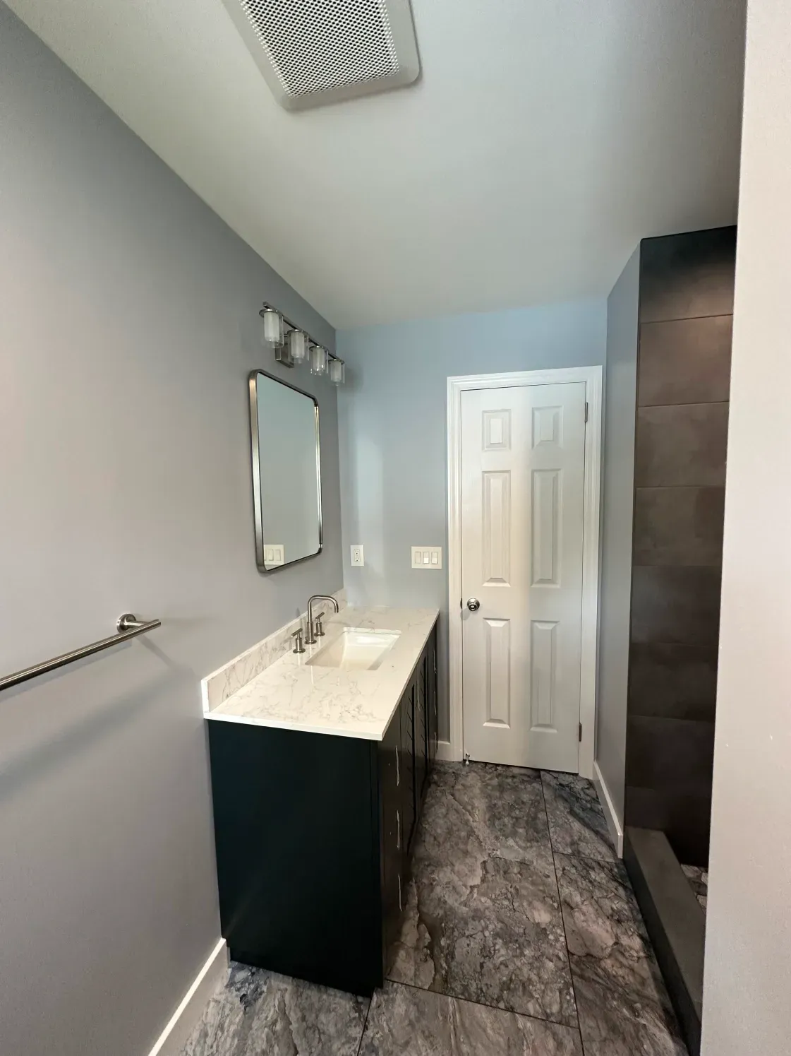 Bathroom with blue walls, dark vanity, white countertop, and patterned floor tiles.