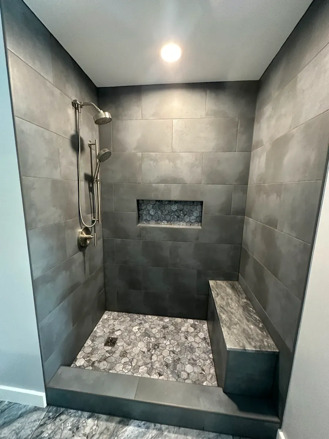 Gray tiled shower with bench, pebble floor, showerhead, and recessed shelf.
