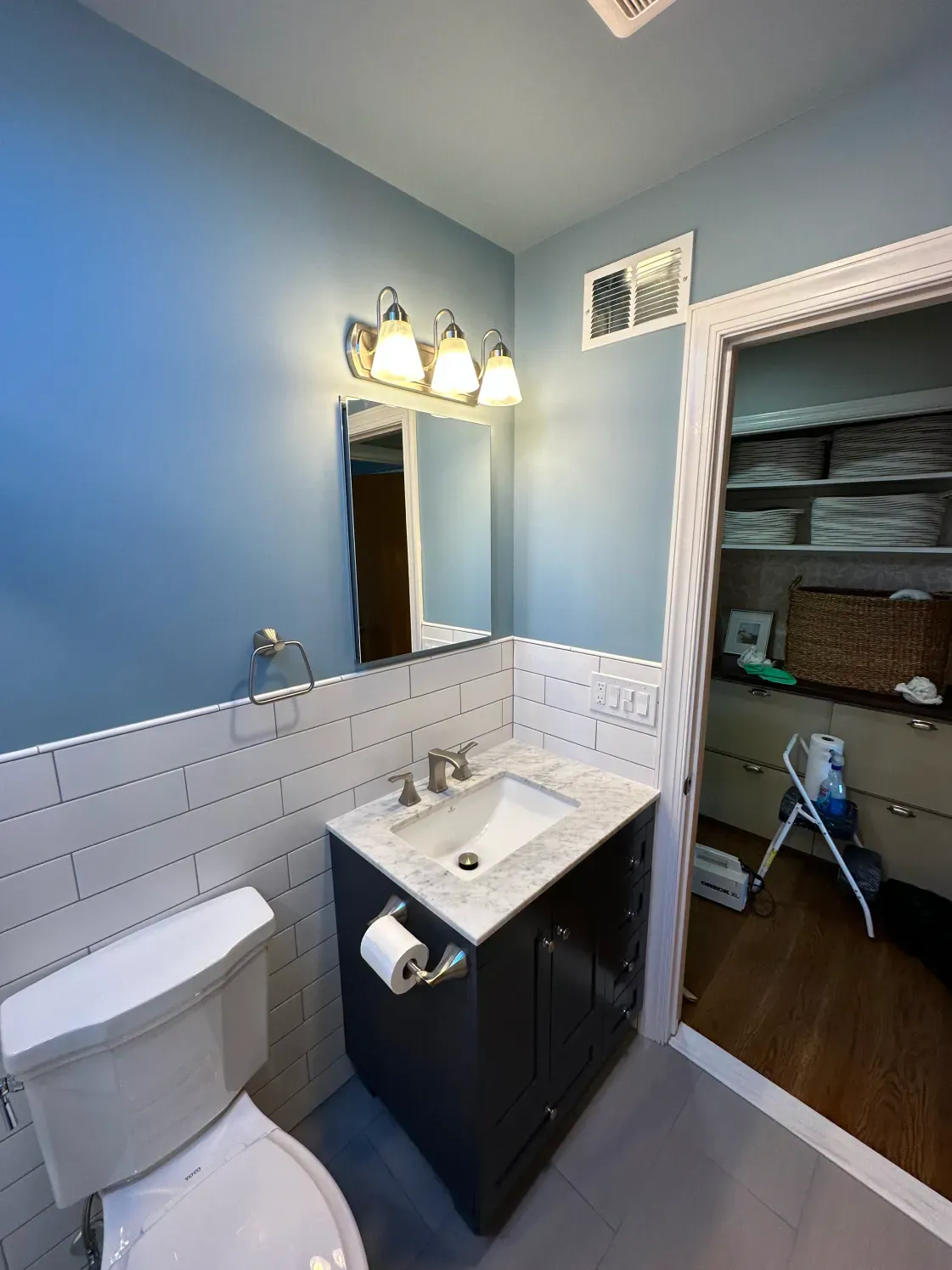 Blue bathroom with white tile, navy vanity, and a closet to the side.