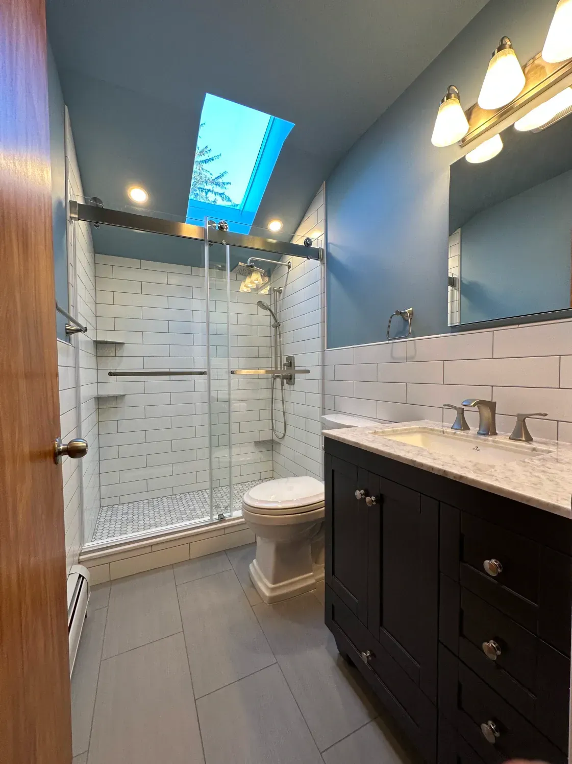 Bathroom with a skylight, shower, dark vanity, white and gray tiles, and blue walls.