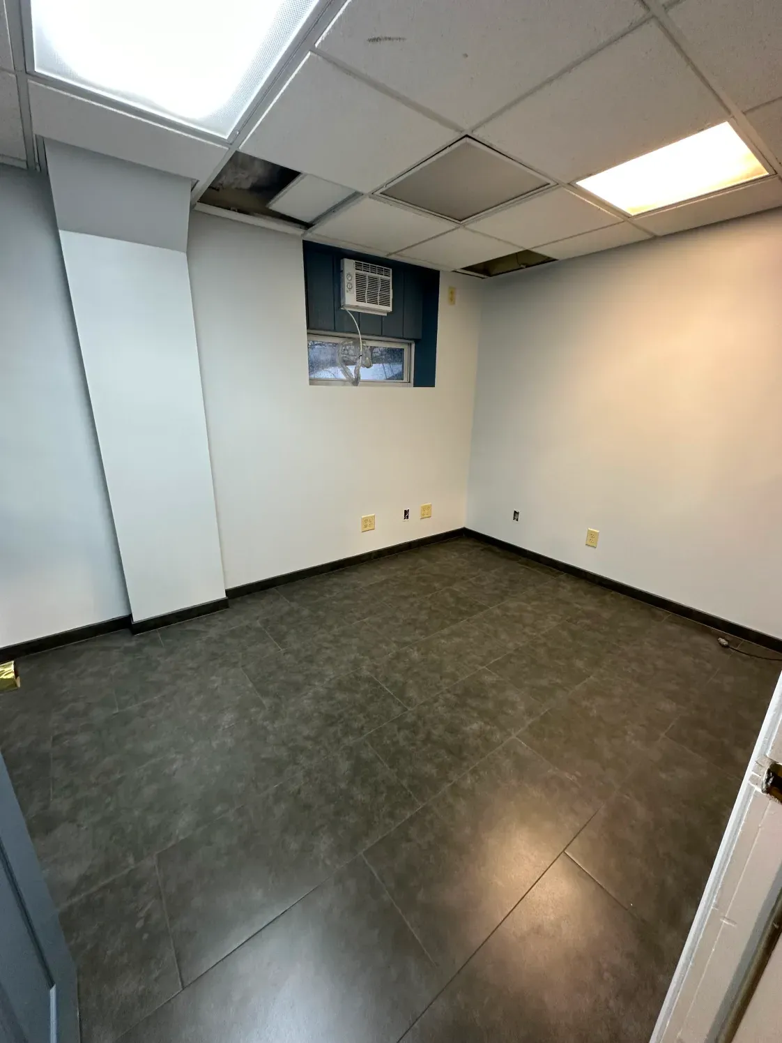 Empty office room with dark floor, white walls, and a small window.
